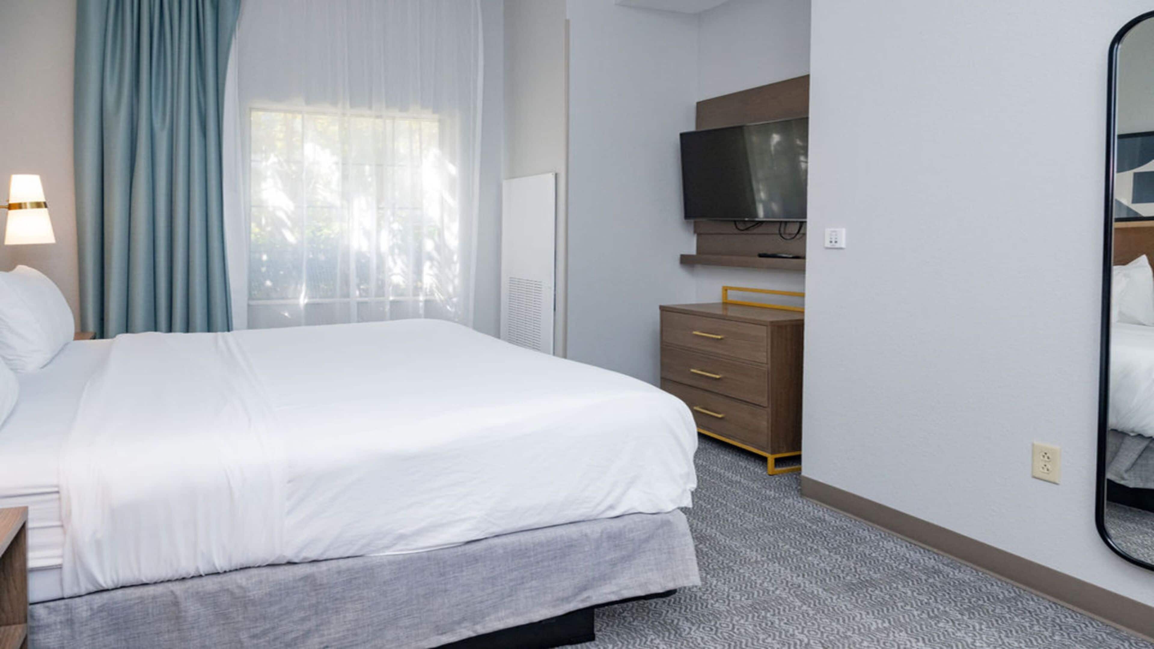 Une chambre d’hôtel avec un grand lit, une commode, un miroir et un téléviseur.