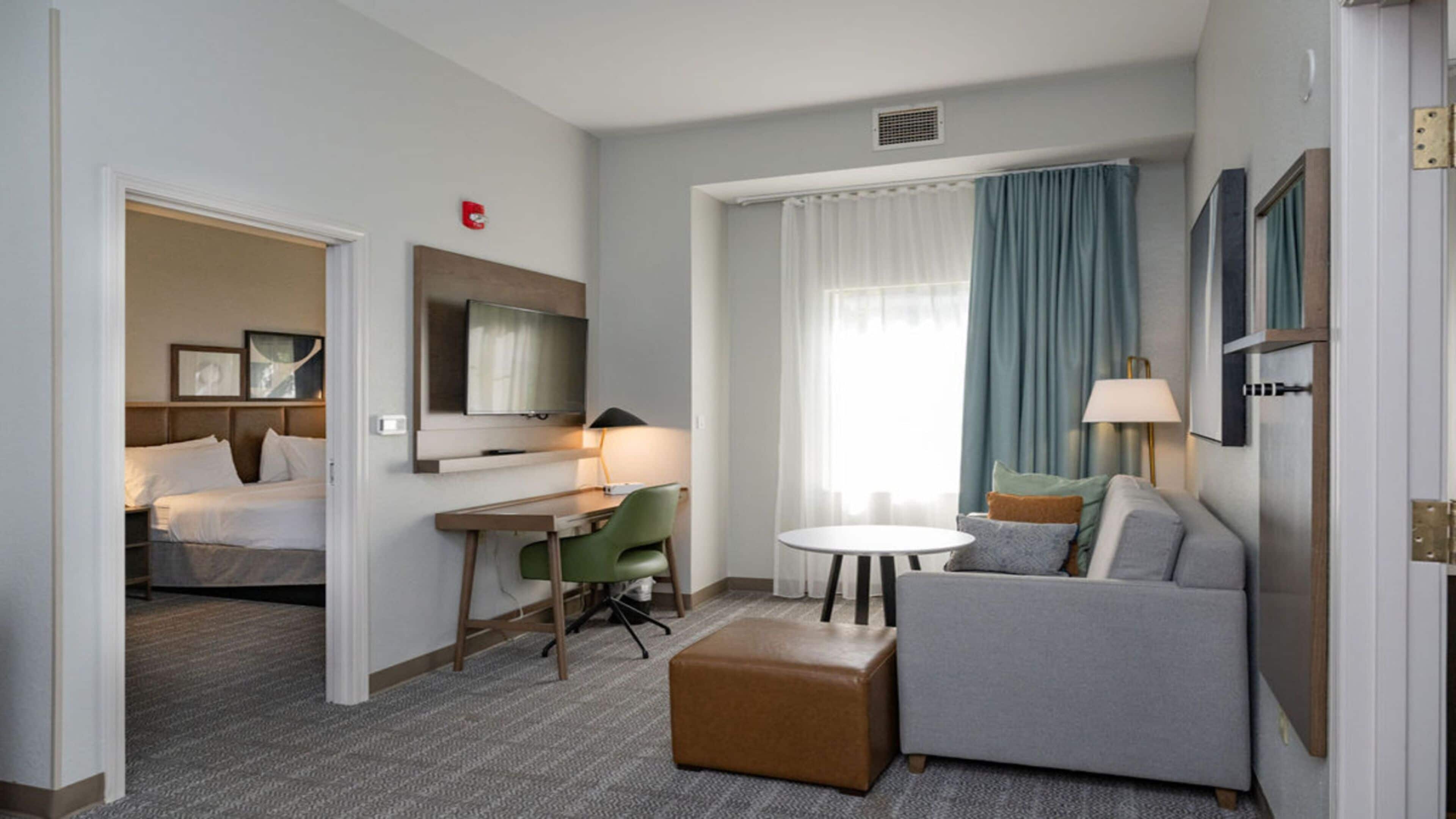 Habitación de hotel con cama, escritorio, silla, sofá, mesita y televisor.