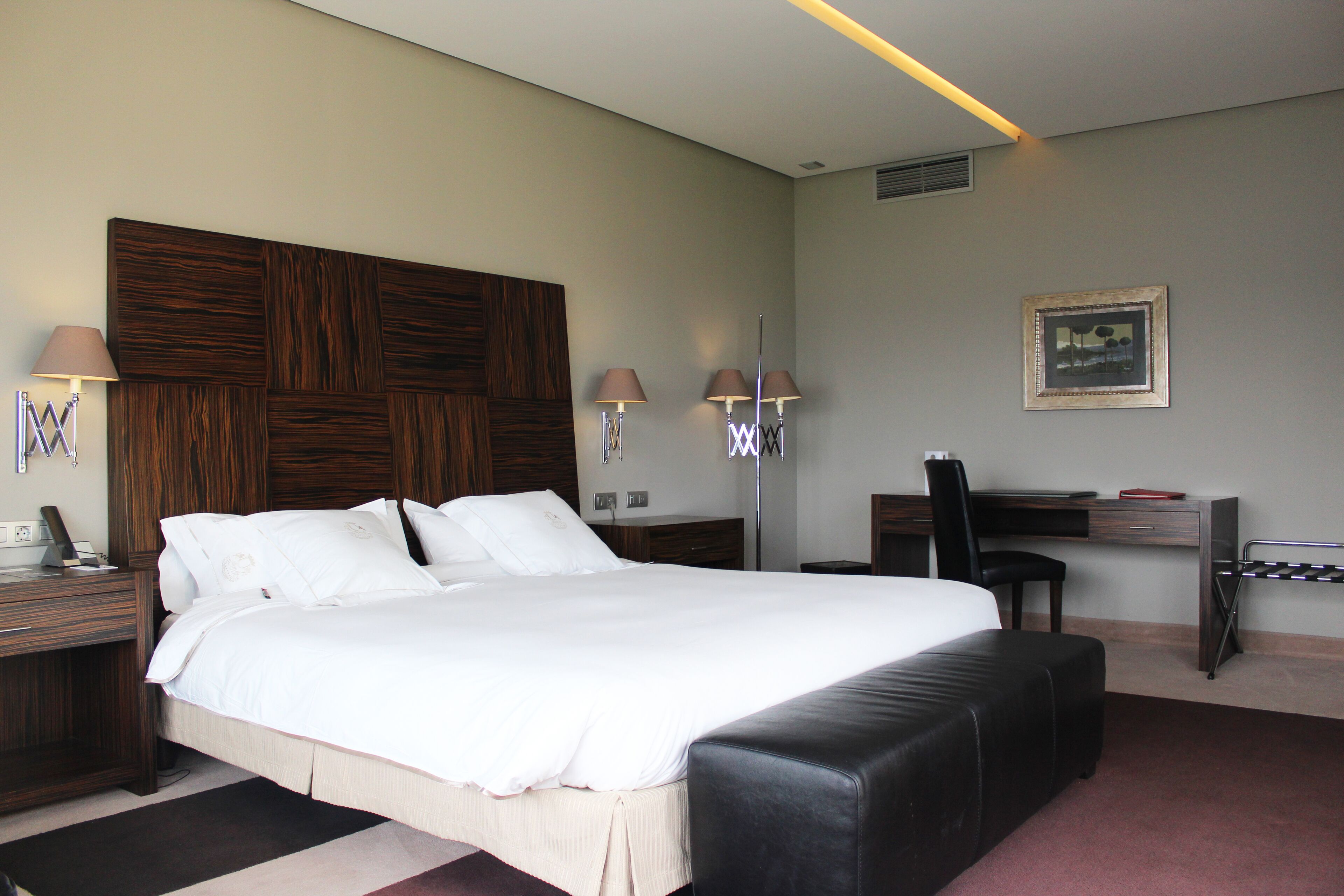 A hotel room with a large bed, a desk, a chair, and two lamps.