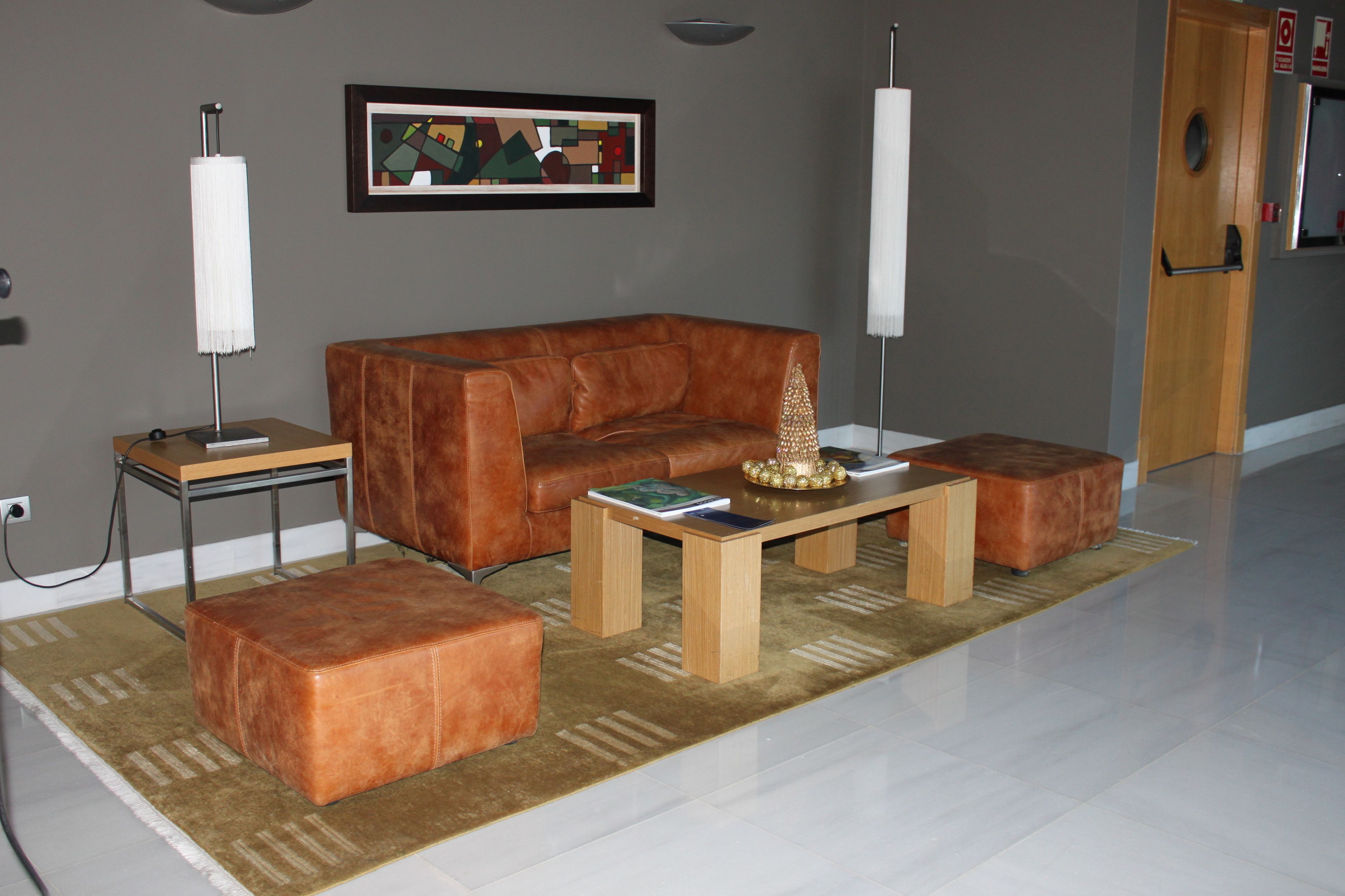 Una sala de estar con un sofá de cuero marrón, dos otomanes a juego, una mesa de centro de madera y un cuadro abstracto enmarcado en la pared.