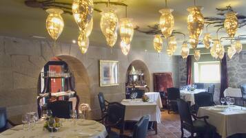 A restaurant interior with multiple round tables, chairs, and hanging crystal chandeliers.