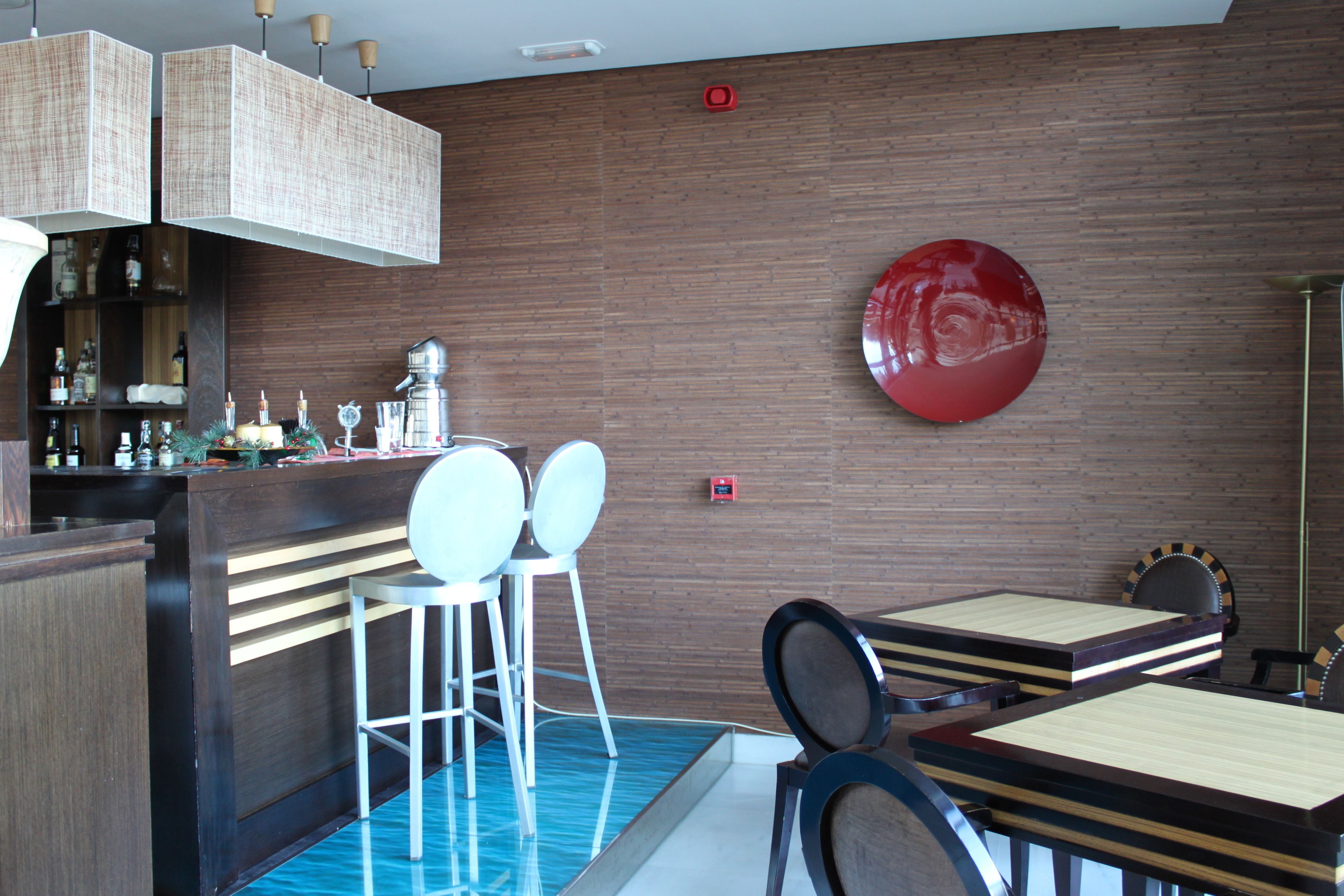 A bar area with stools, a counter with bottles, and a red decorative element on the wall.