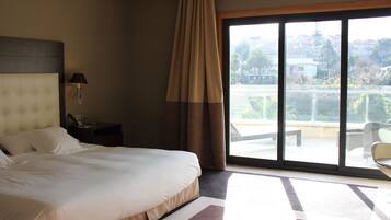 Habitación de hotel con una cama grande, una mesita de noche, una lámpara y vistas al exterior a través de una puerta corrediza de vidrio.