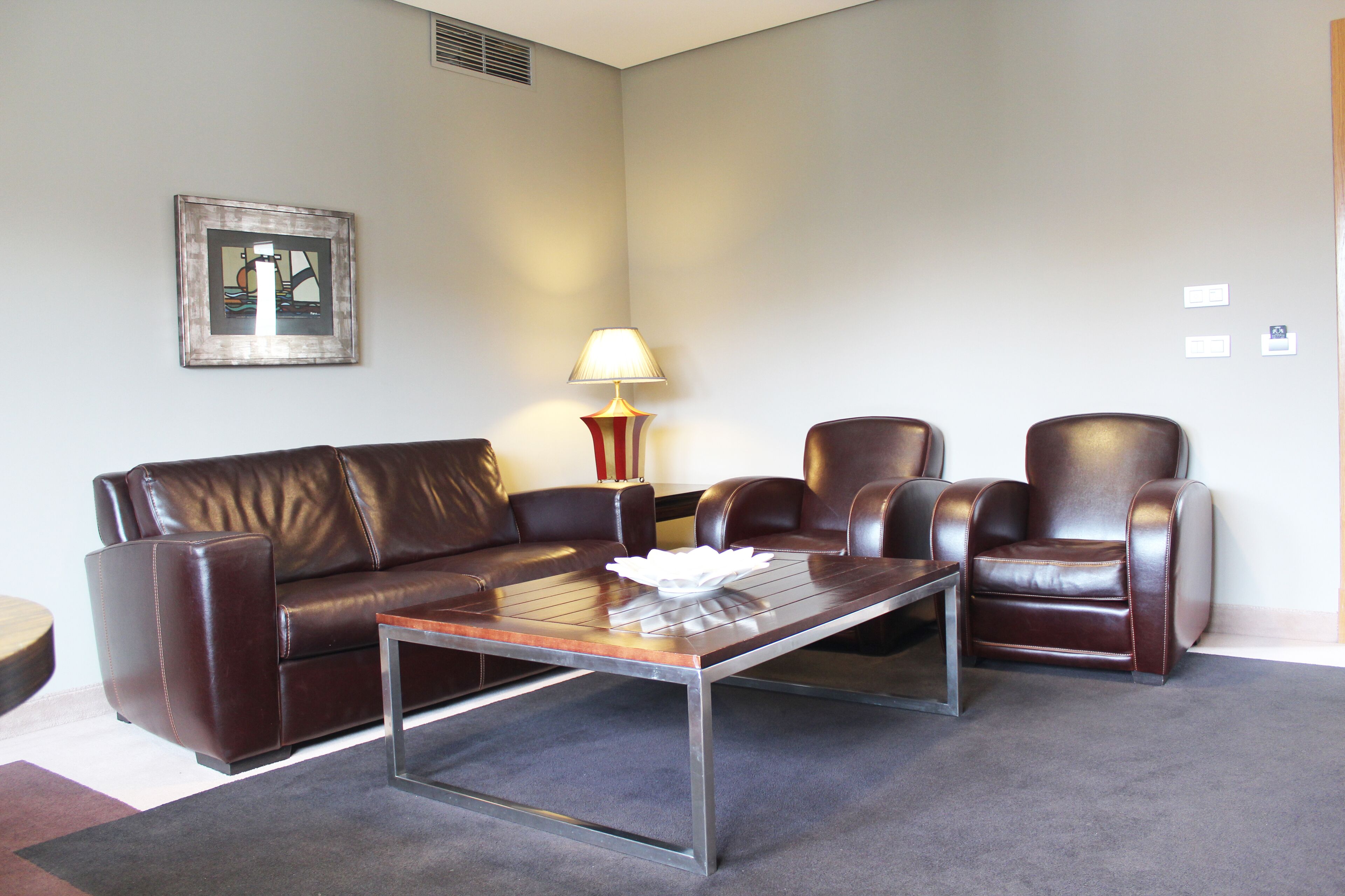 A living room with a brown leather sofa, two leather armchairs, a wooden coffee table, and a floor lamp.