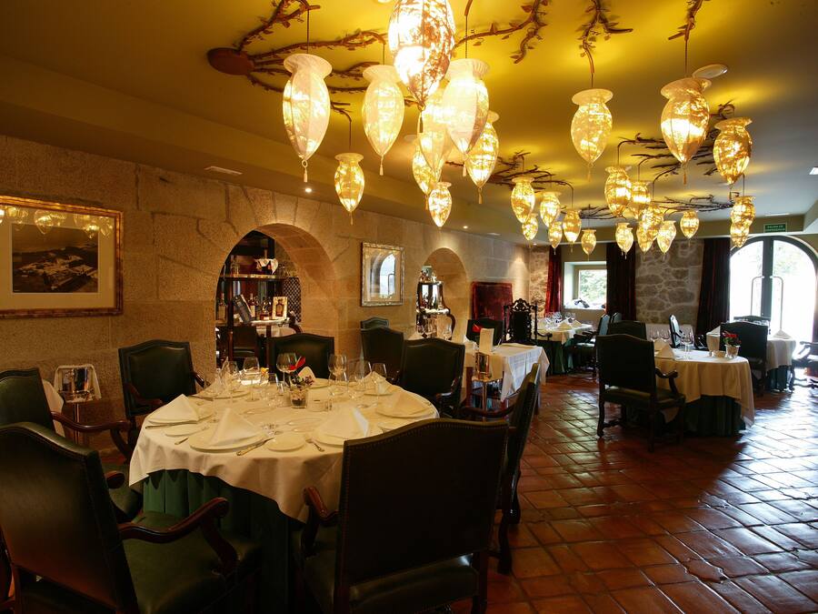 Un comedor con mesas redondas dispuestas para una comida, con candelabros y paredes de piedra.