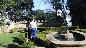 Un jardín con una fuente, setos cuidados y una estatua.