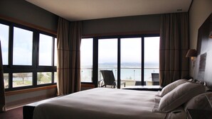 Hotelkamer met een groot bed, een stoel, een tafel en uitzicht op de stad en bergen door grote ramen.