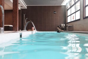 Una piscina interior con agua cristalina, un trampolín y una pared de azulejos.