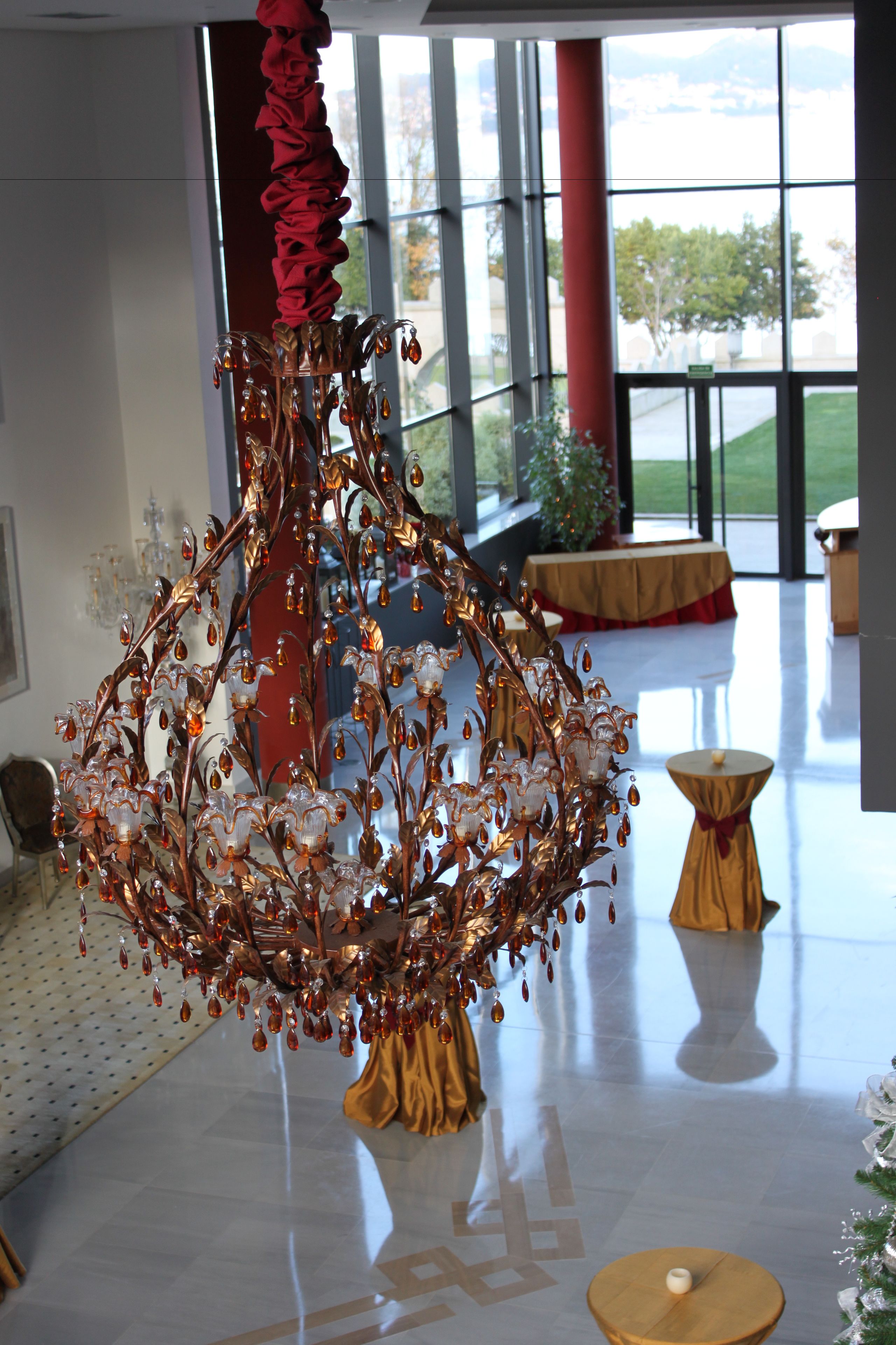 Un candelabro con diseño rojo y dorado en un vestíbulo amplio con ventanas grandes y vistas al exterior.