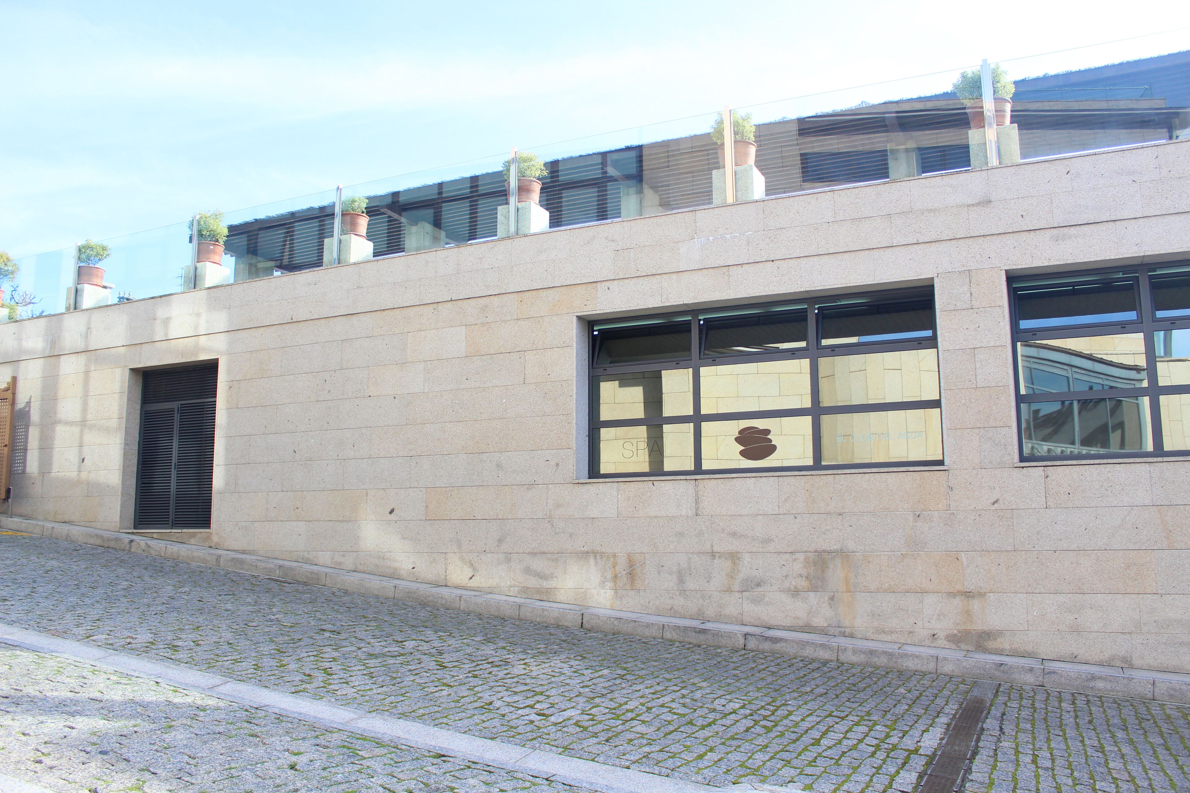 Un bâtiment doté d’une façade en pierre, de grandes fenêtres et de plantes en pot sur le toit.