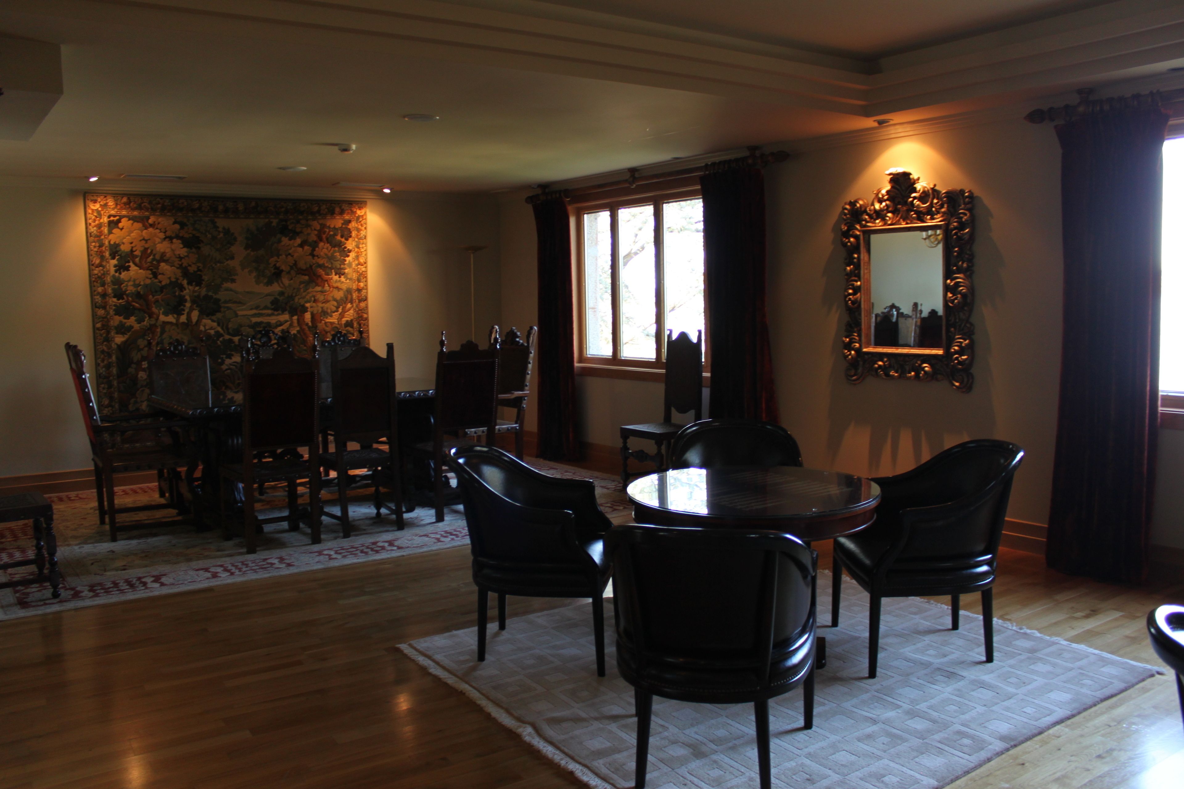 A dining room with a round table, black chairs, a tapestry, and a mirror on the wall.