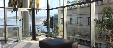 Un intérieur moderne avec de grandes fenêtres, un pouf noir et une vue sur une zone côtière.