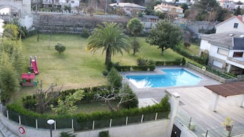 Enjoy a serene garden with a swimming pool, play area, and wooden deck, surrounded by a stone wall and offering a view of neighboring homes.