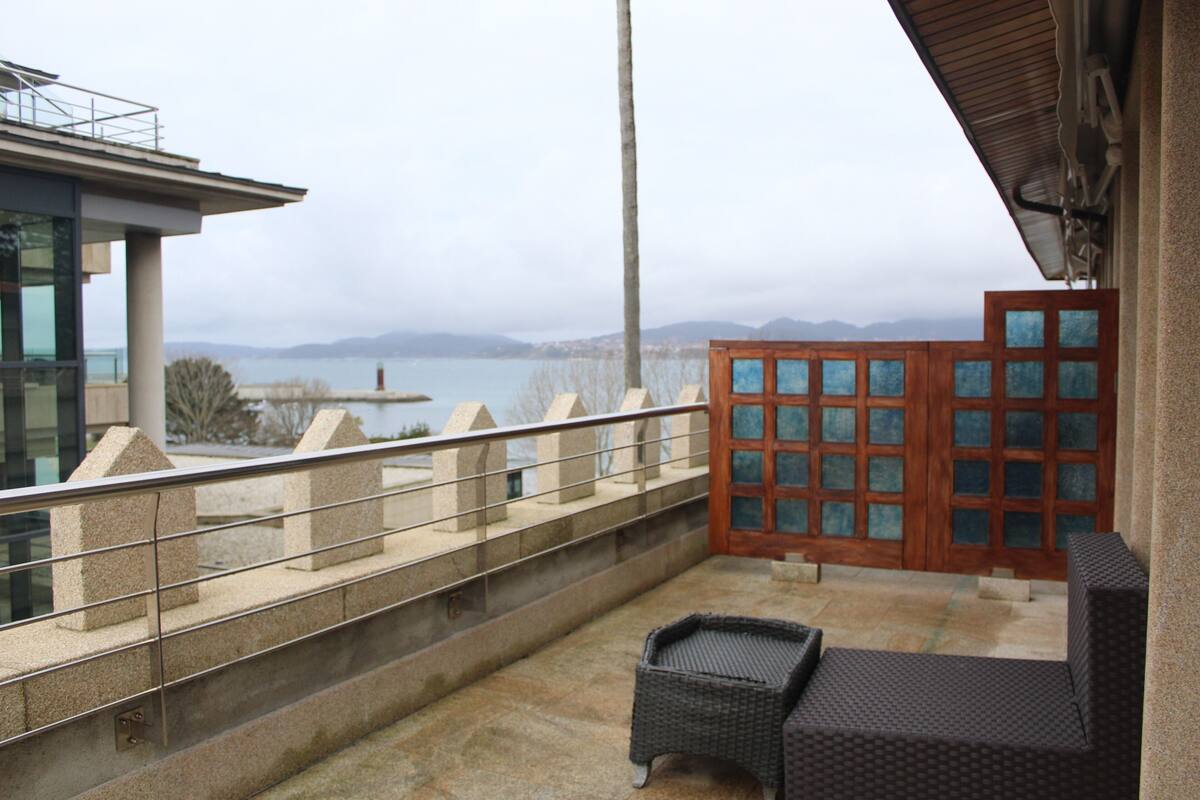 A balcony with a view of the sea, a wooden door with glass panels, and a wicker chair.