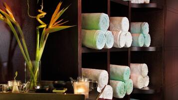 A neatly organized shelf with neatly rolled towels in various colors, a glass vase with a plant, and a candle on a tray.