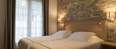 A double bed with a wooden headboard, a stone-patterned wall, and a nightstand with a lamp.