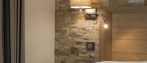 A hotel room with a stone wall, a bedside table with a tray holding a cup and cookies, and a wooden headboard.