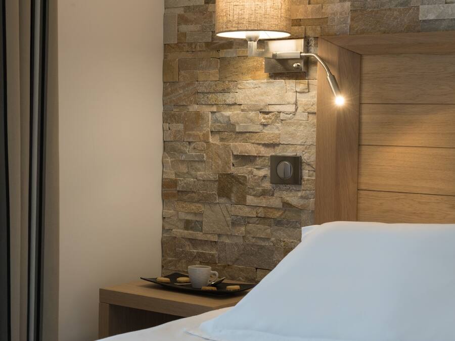 Ein Hotelzimmer mit Steinwand, einem Nachttisch mit Tablett, auf dem eine Tasse und Kekse stehen, und einem Holz-Kopfteil.