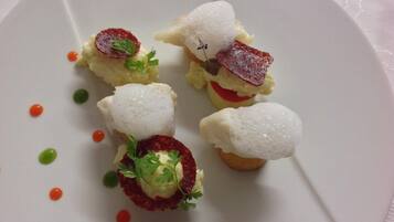 A white plate with four food items, each topped with a piece of meat and garnished with parsley.