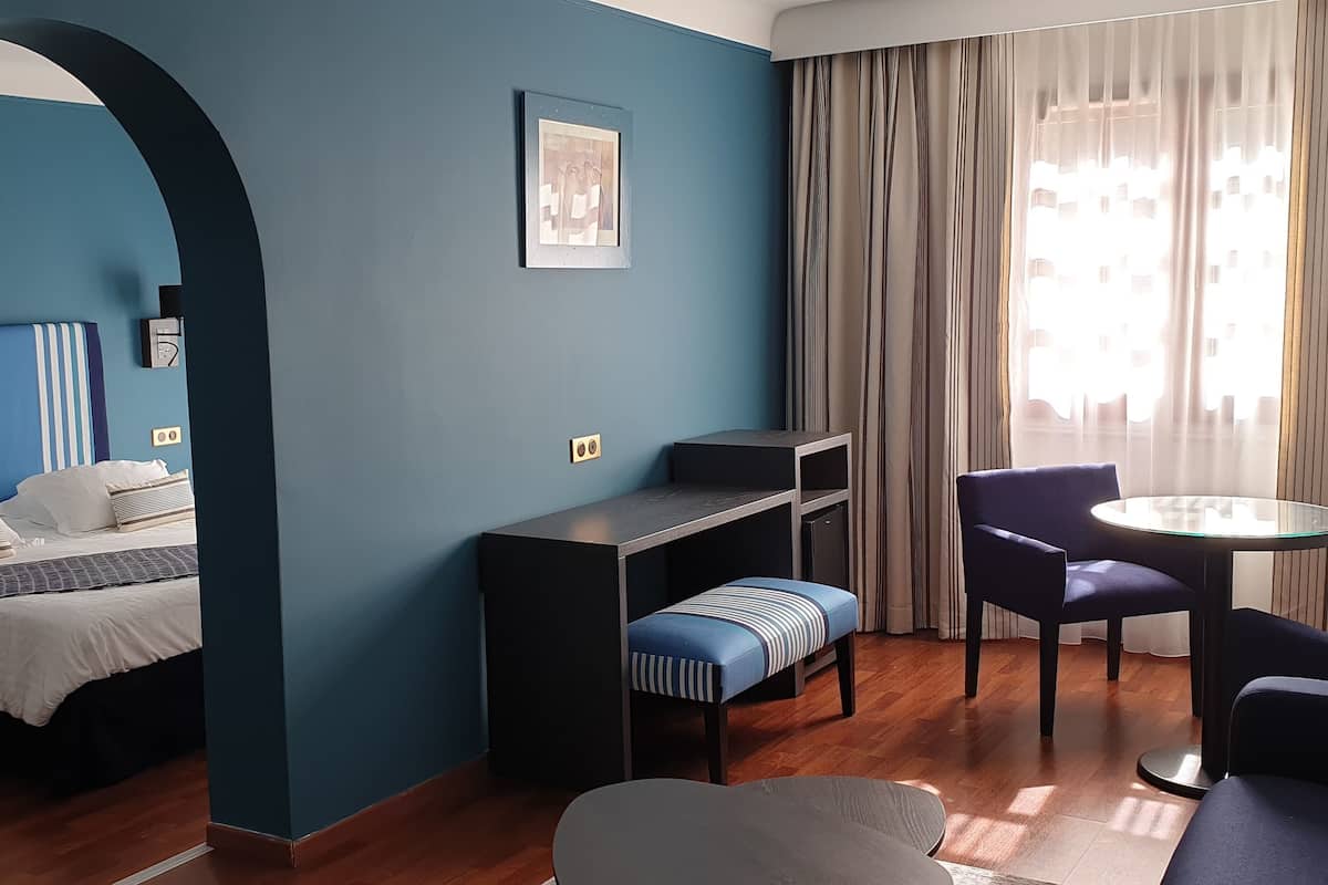 A modern hotel room with a bed, a desk, a chair, and a sofa.