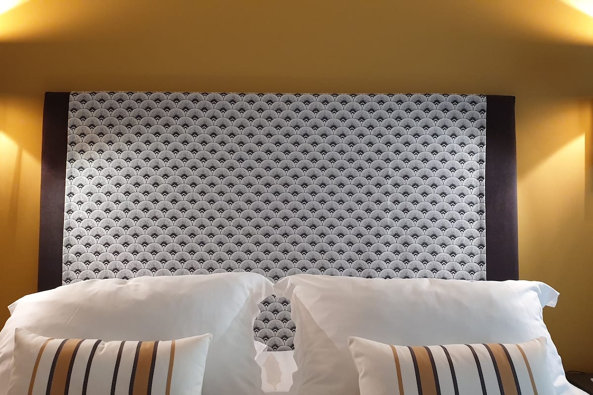 A hotel room with a patterned headboard, two bedside lamps, and a bed with white and striped pillows.