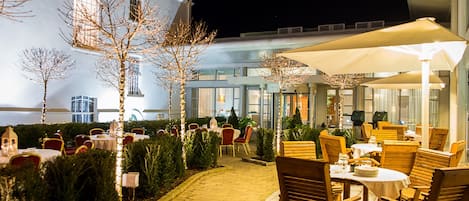 An outdoor dining area with tables and chairs, a pathway, and a building in the background.