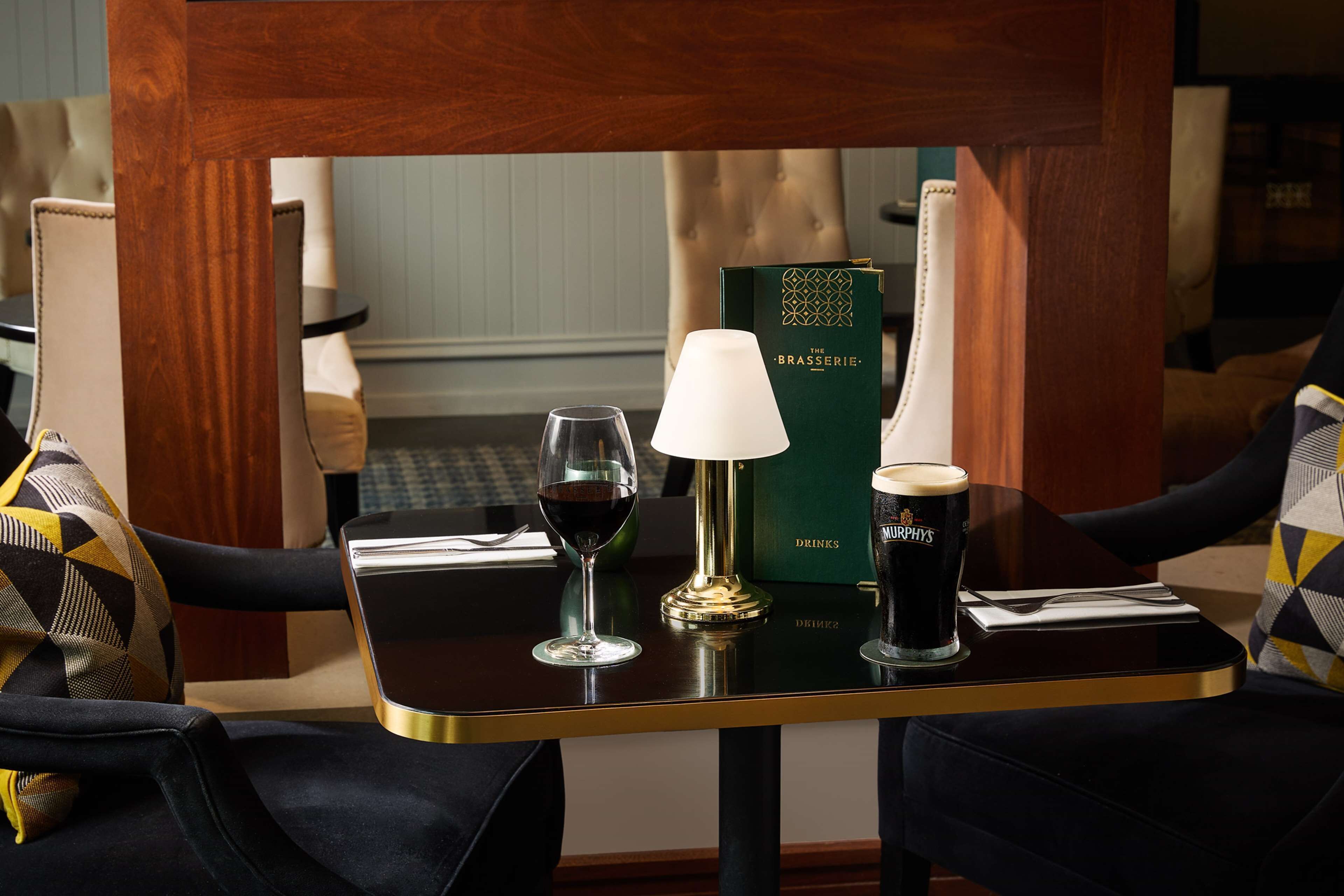 A table with a book titled 'The Brasserie', two wine glasses, a lamp, and a coffee cup.
