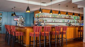 A bar area with a wooden bar counter, multiple hanging pendant lights, and striped bar stools.