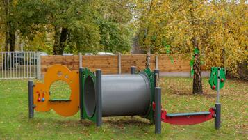 A playground with a cylindrical climbing structure, a seesaw, and a swing set.