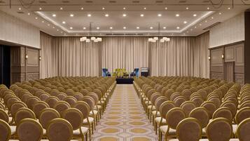 A conference room with rows of chairs, a stage with a podium, and a large curtain backdrop.