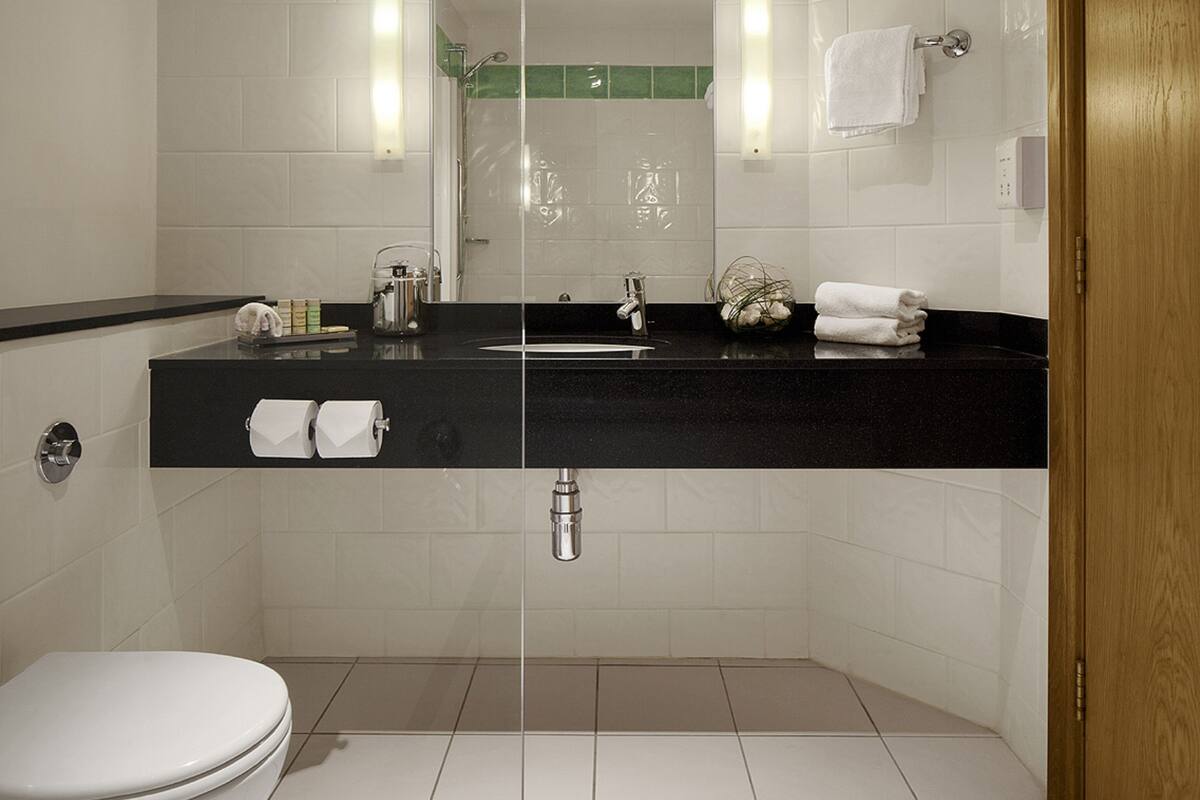 Un baño moderno con cabina de ducha de vidrio, encimera negra y azulejos blancos.
