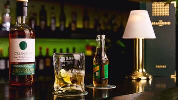 Un bar avec une bouteille de Green Spot, un verre rempli de glace et un quartier de citron vert, et une bouteille de bière.