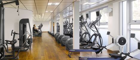 A gym with exercise equipment, wooden flooring, and large windows.