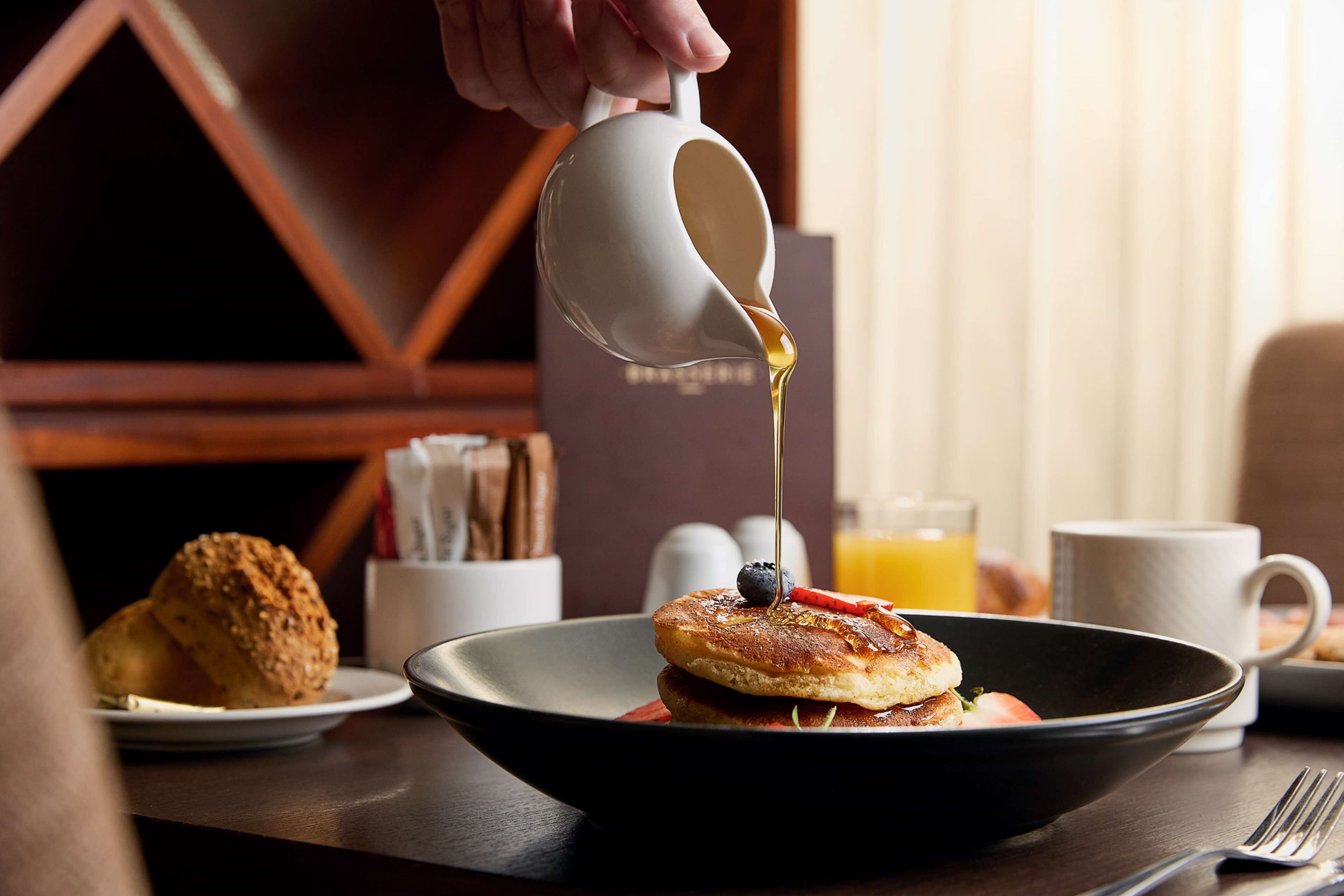 Un desayuno con tortitas, almíbar y un vaso de zumo de naranja sobre una mesa.