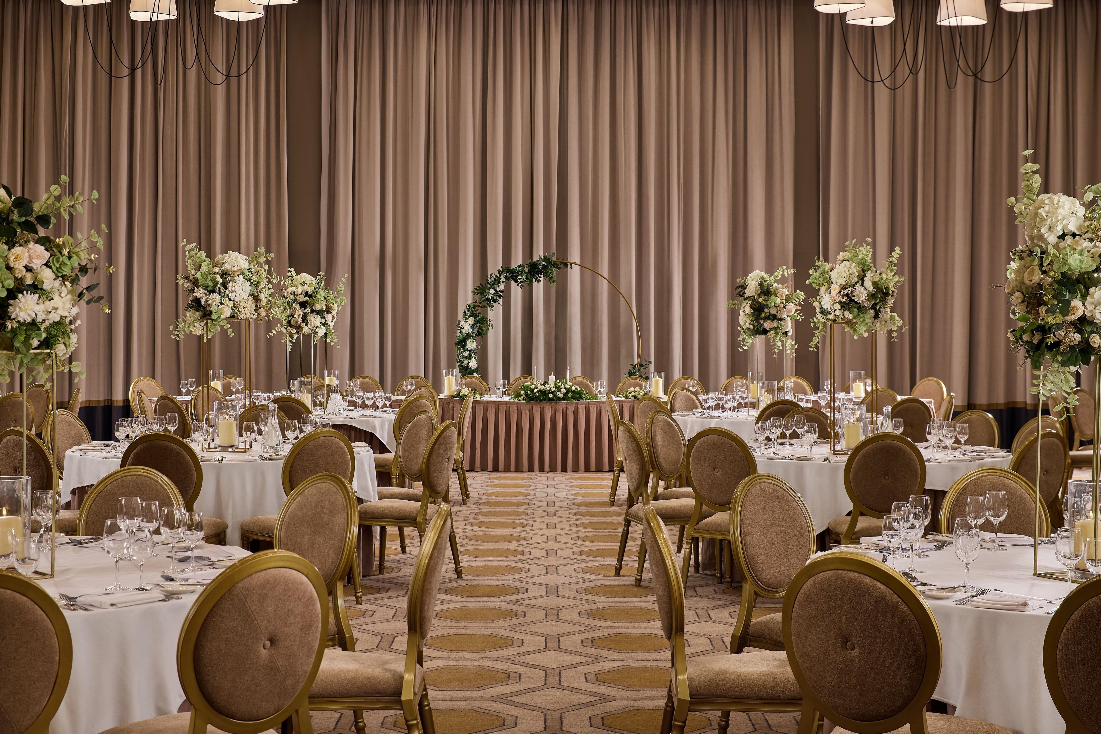 Een balzaal met ronde tafels, stoelen en bloemdecoraties.