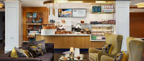 A modern hotel lobby with a reception area, seating arrangements, and a coffee bar.