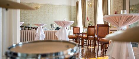 A restaurant with tables covered in white tablecloths, wooden chairs, and a drum in the foreground.