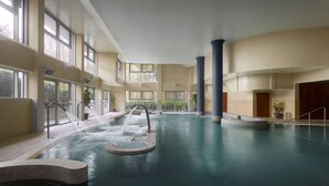 Piscina interna com vários pontos de acesso, janelas amplas e um elemento aquático central.