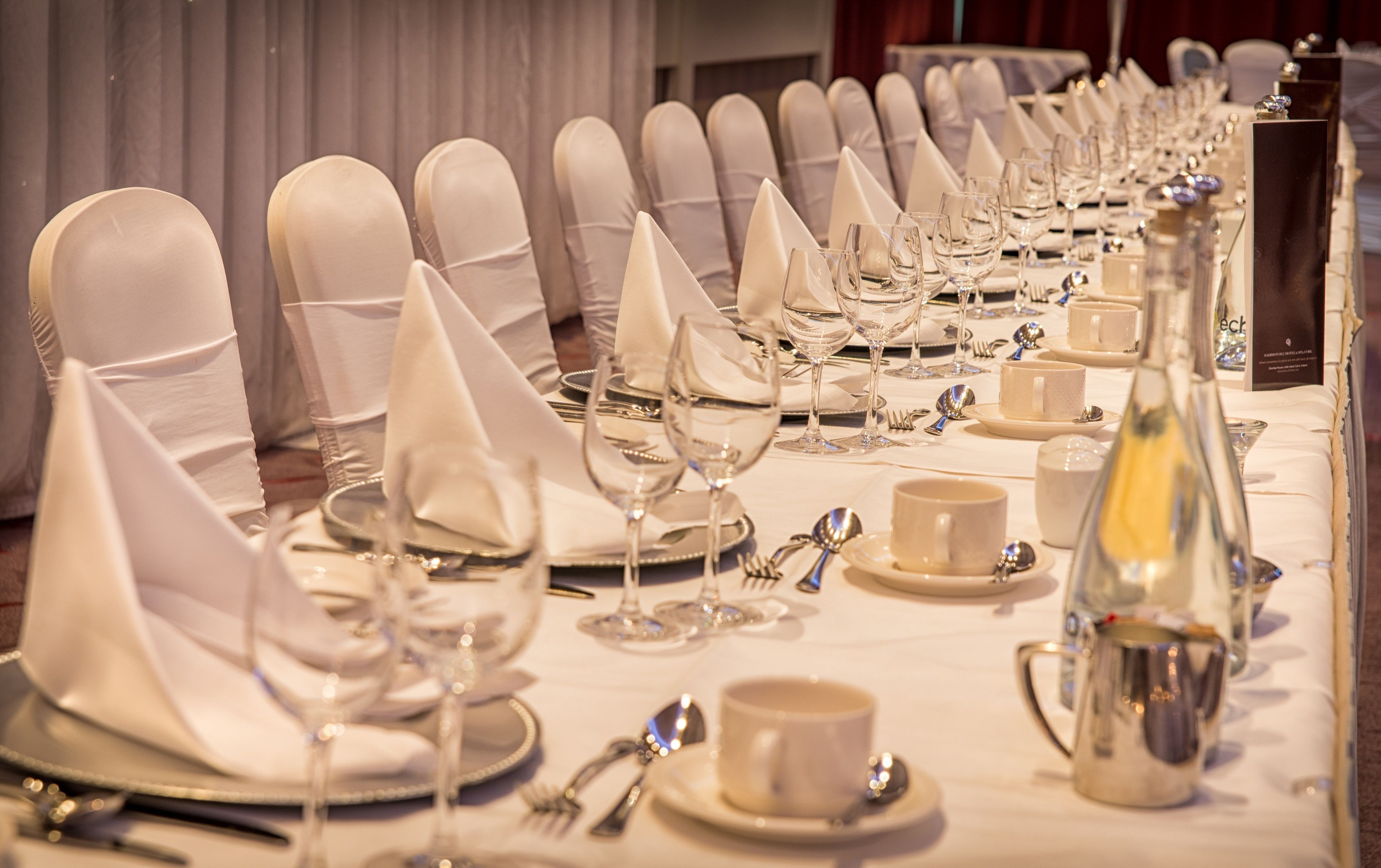 A banquet table set with white napkins, silverware, and glassware, indicating a formal dining arrangement.