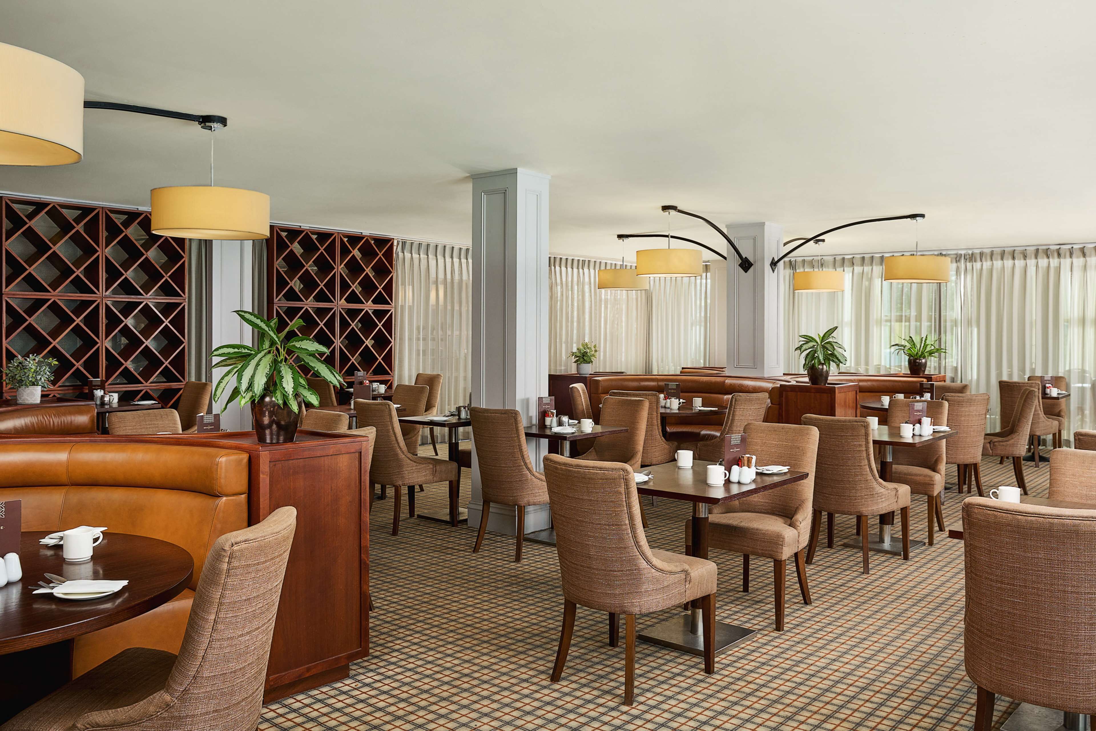 A hotel dining area with booths, tables, and chairs, featuring a checkered floor pattern and pendant lighting.