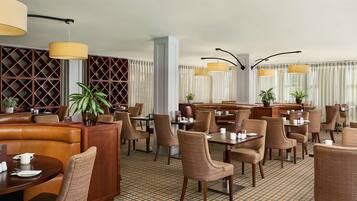 A hotel dining area with booths, tables, and chairs, featuring a checkered floor pattern and pendant lighting.