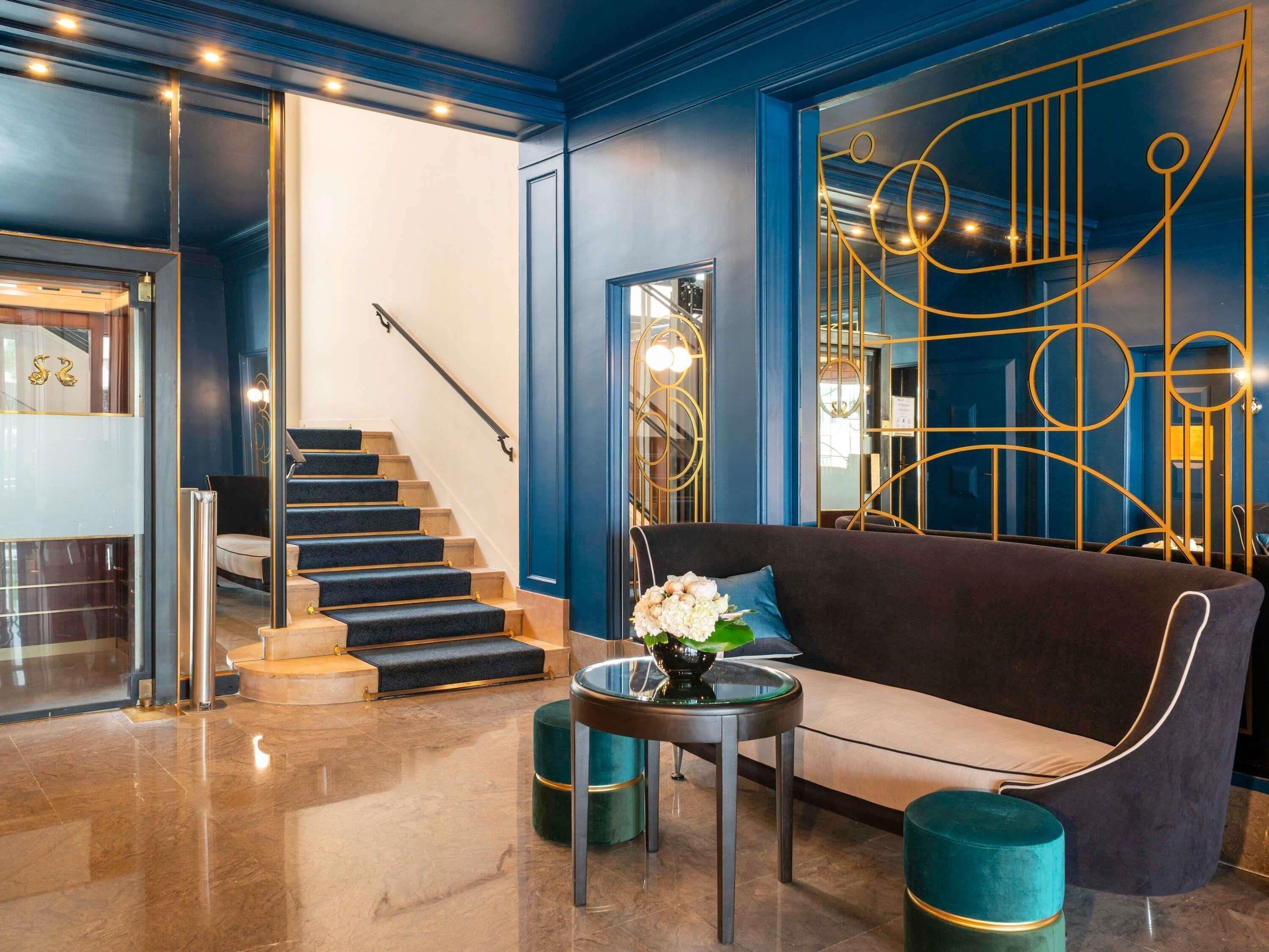 A modern lobby with a staircase, a dark-colored sofa, and a glass table with a vase of flowers.