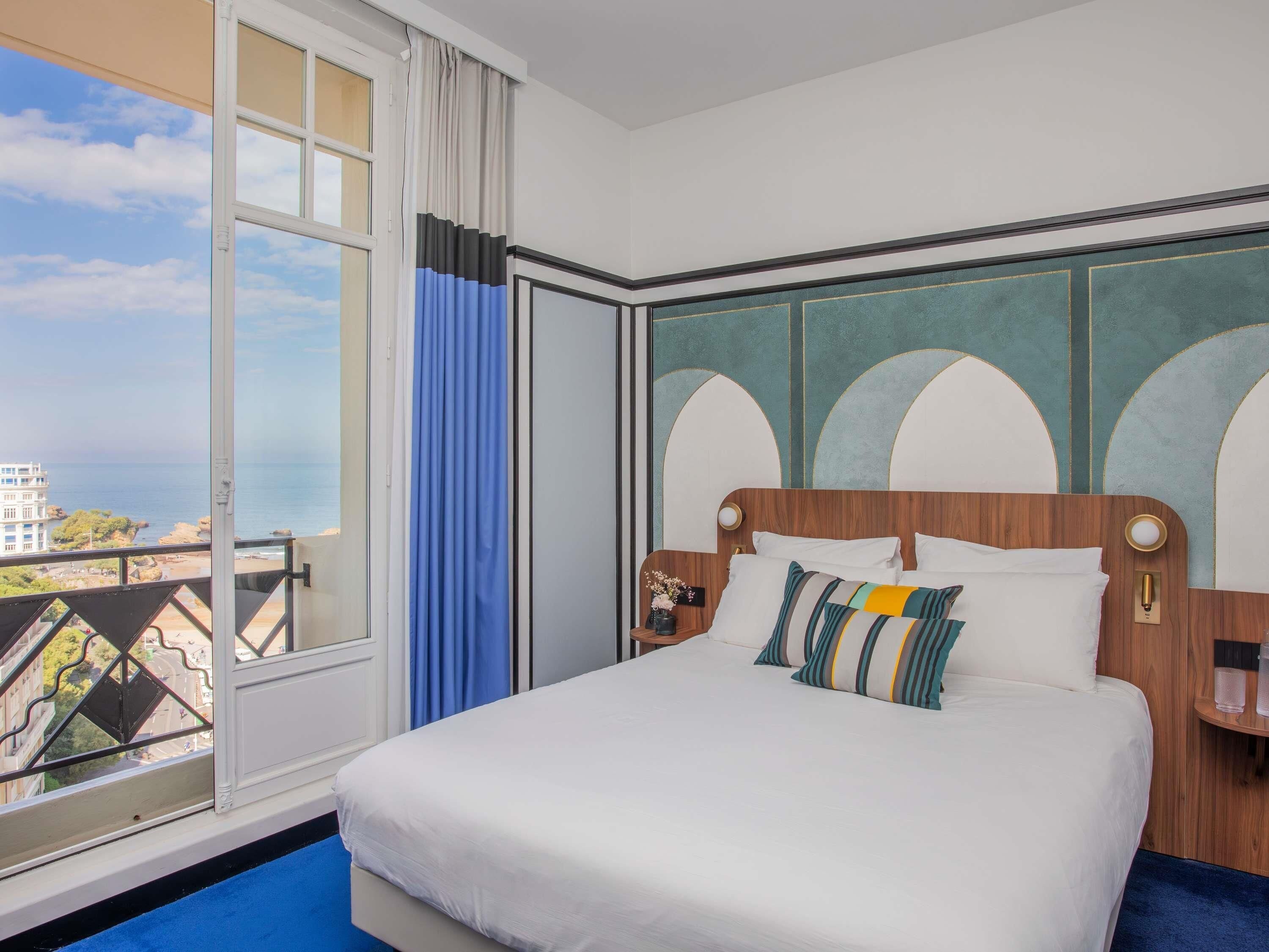 A hotel room with a large bed, a view of the sea, and a balcony.