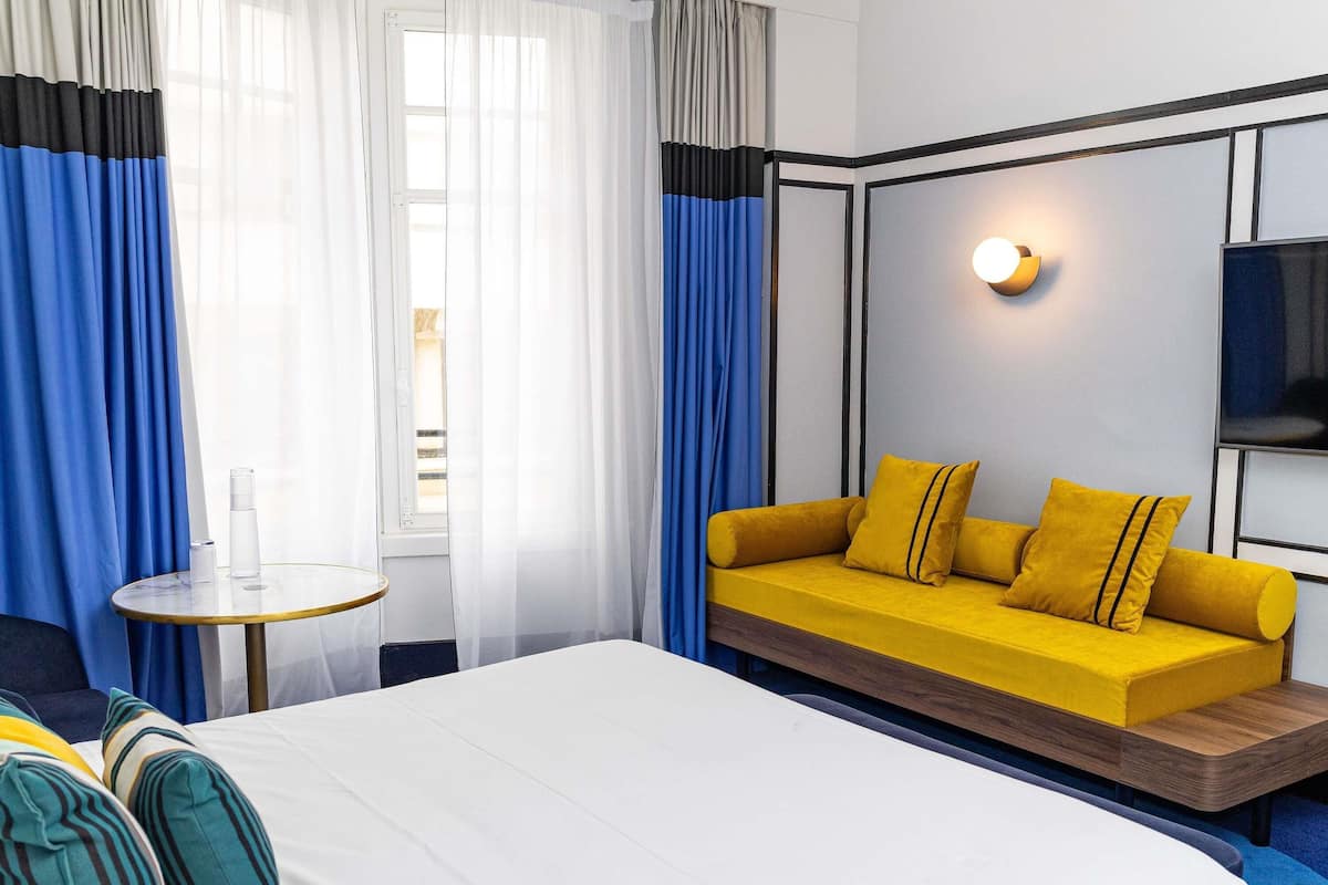 A hotel room with a bed, a sofa, a small round table, and a wall-mounted light.