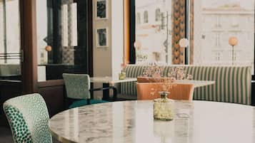 Een ronde tafel met stoelen, een vaas met bloemen en uitzicht op gebouwen door grote ramen.