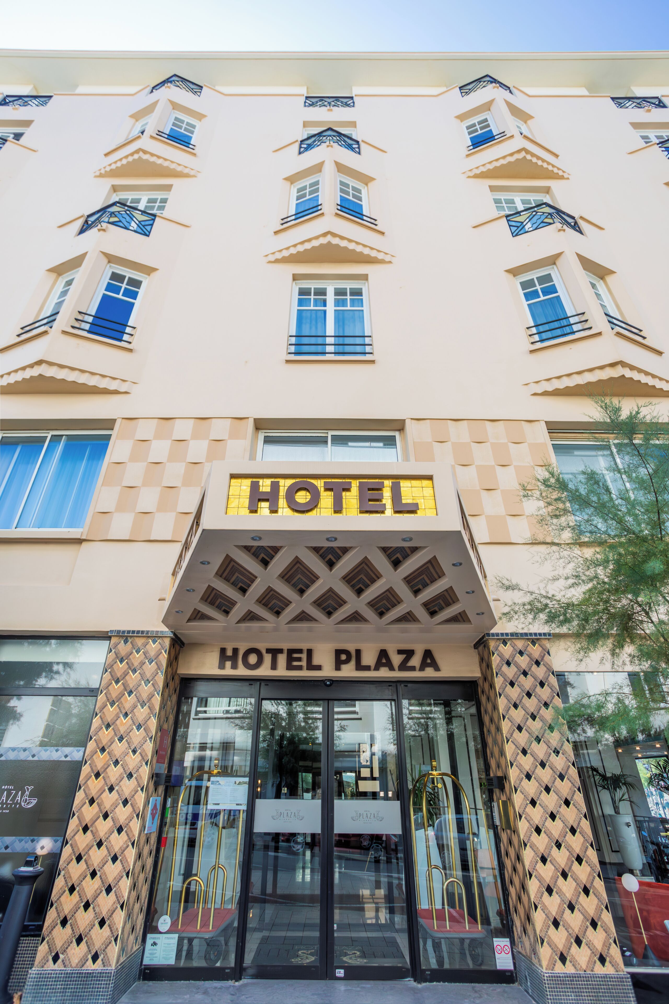 A hotel facade with a checkered pattern, a prominent 'HOTEL' sign, and a 'HOTEL PLAZA' sign above the entrance.