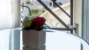 A window view of a beach with a railing, a glass table with a vase of flowers, and a clear sky.