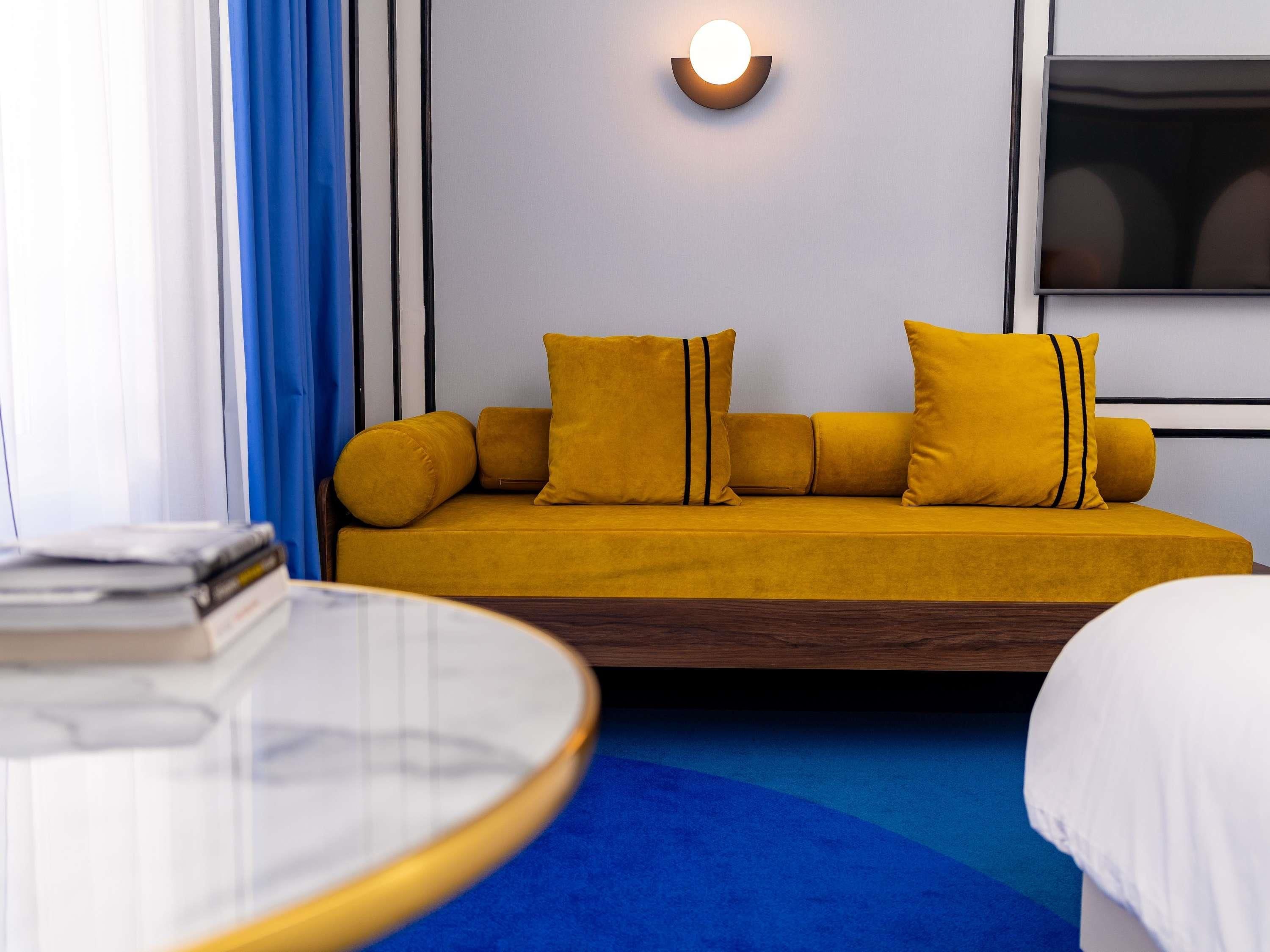 A hotel room with a sofa, a round table, and a wall-mounted TV.