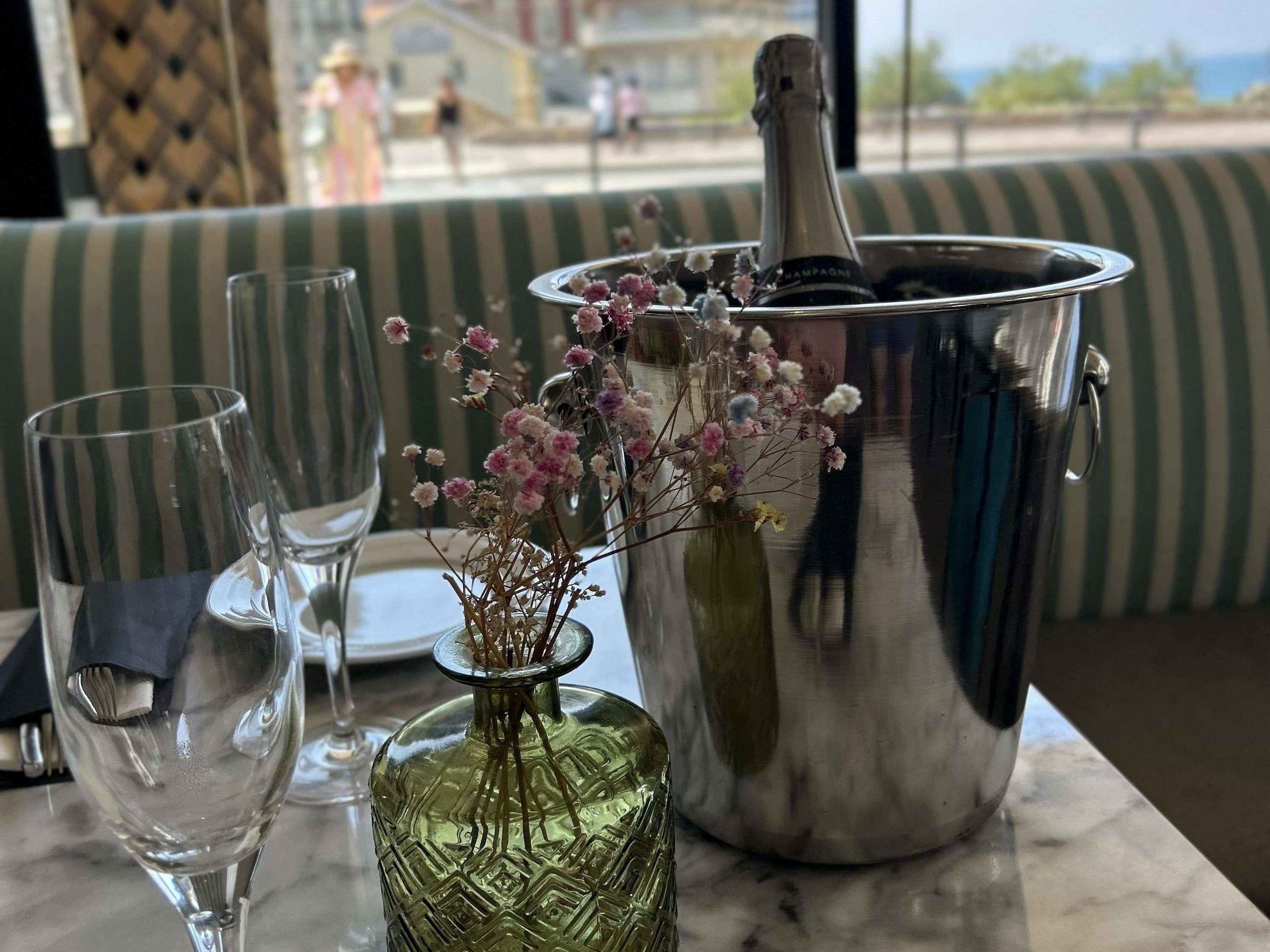 Una mesa con una botella de champán, un florero con flores y dos copas.