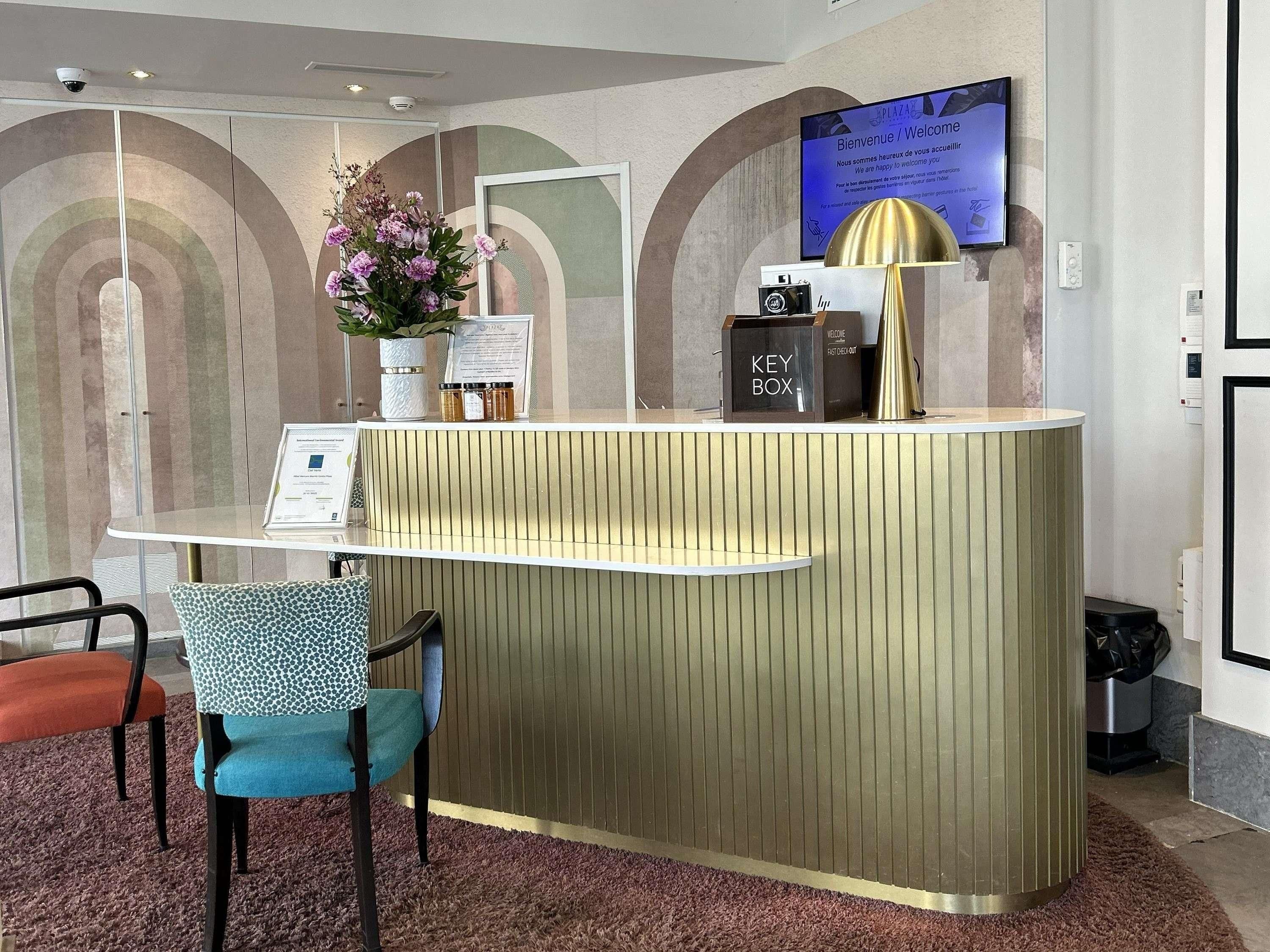 A reception desk with a key box, a welcome sign, a potted plant, and a television screen.